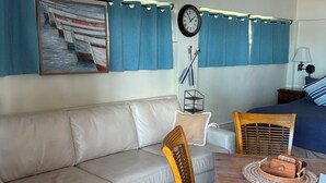 Una stanza accogliente con un divano color beige, un tavolo da pranzo in legno con sedie, una sveglia e un quadro raffigurante barche sulla parete.