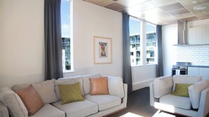 A modern living room with a sofa and armchair, a coffee table, and a kitchen area with a stove. - Liberty Apartment Hotel (Wellington)