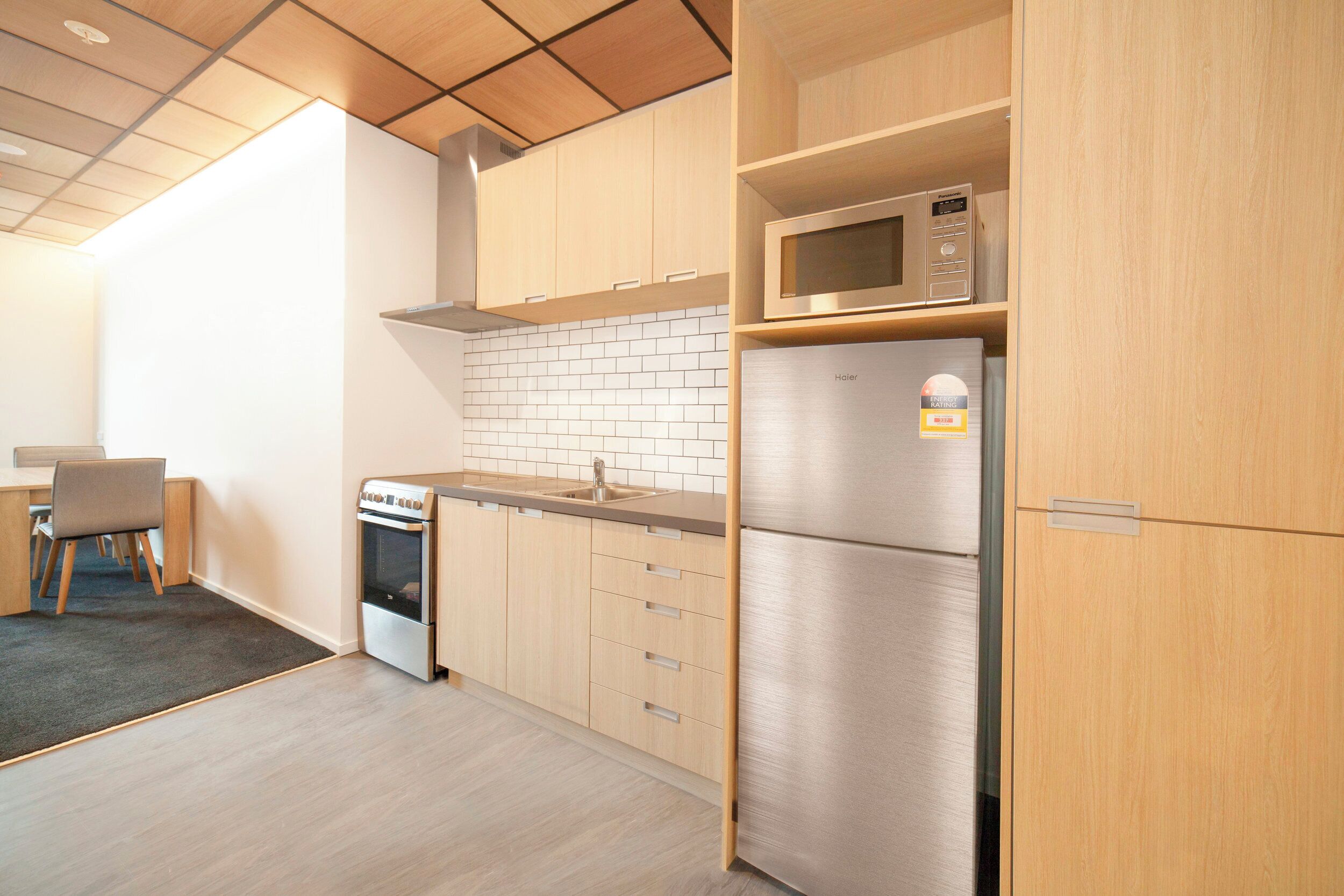 Eine moderne Küche mit Holzausstattung, einem Edelstahlkühlschrank, einer Mikrowelle und einem Einbauofen.