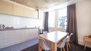 A modern kitchen with white cabinets, a wooden countertop, and a dining area with a table and chairs. - Liberty Apartment Hotel (Wellington)