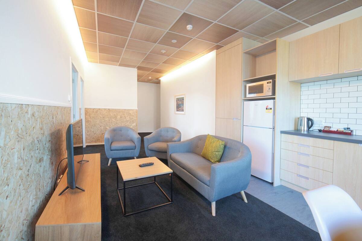 Un salon moderne équipé d’un téléviseur à écran plat, de deux fauteuils, d’un canapé et d’une table basse. Il y a également un coin cuisine avec un four à micro-ondes et un réfrigérateur.