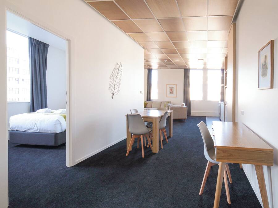 Et hotelværelse med en seng, et spiseområde med bord og stole, samt et lille tekøkken.