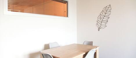 A conference room with a wooden table and four chairs, a window with blinds, and a wall-mounted leaf decoration.