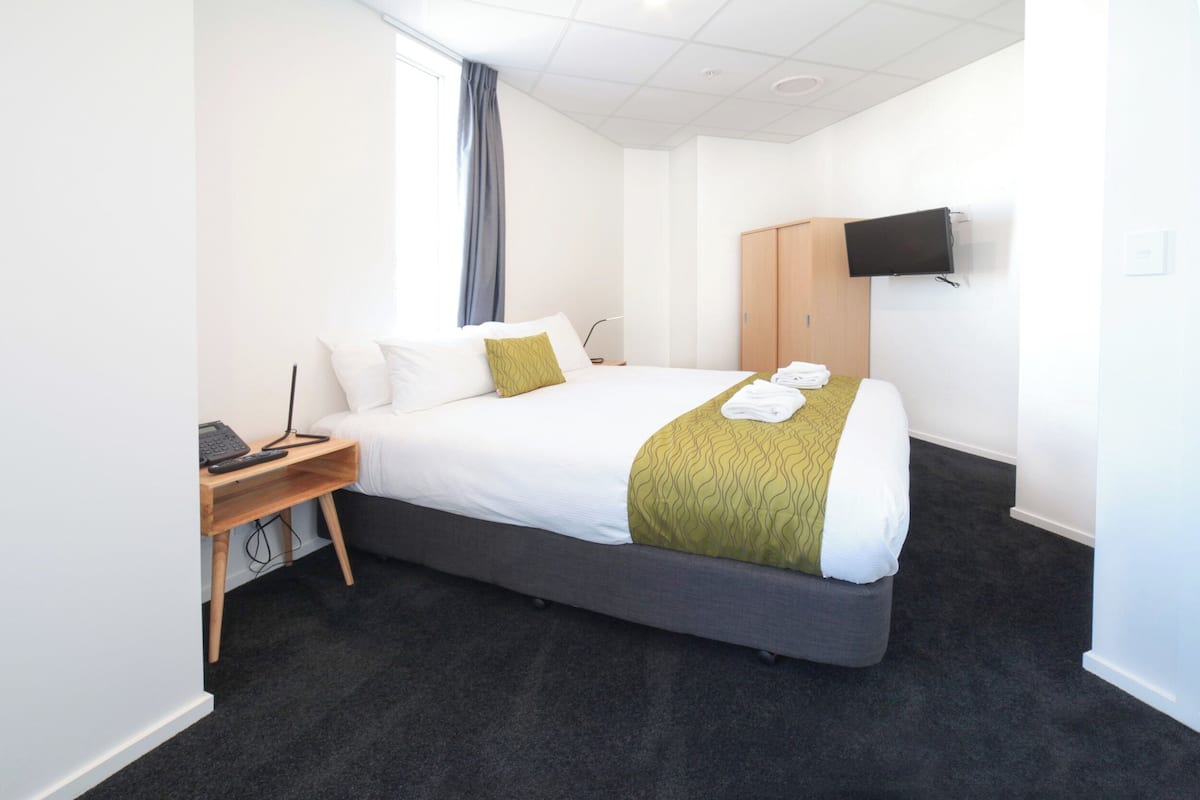 Une chambre d’hôtel avec un grand lit, un bureau avec un ordinateur, un téléviseur fixé au mur et une armoire.
