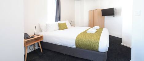 A hotel room with a large bed, a desk with a computer, a TV mounted on the wall, and a wardrobe.