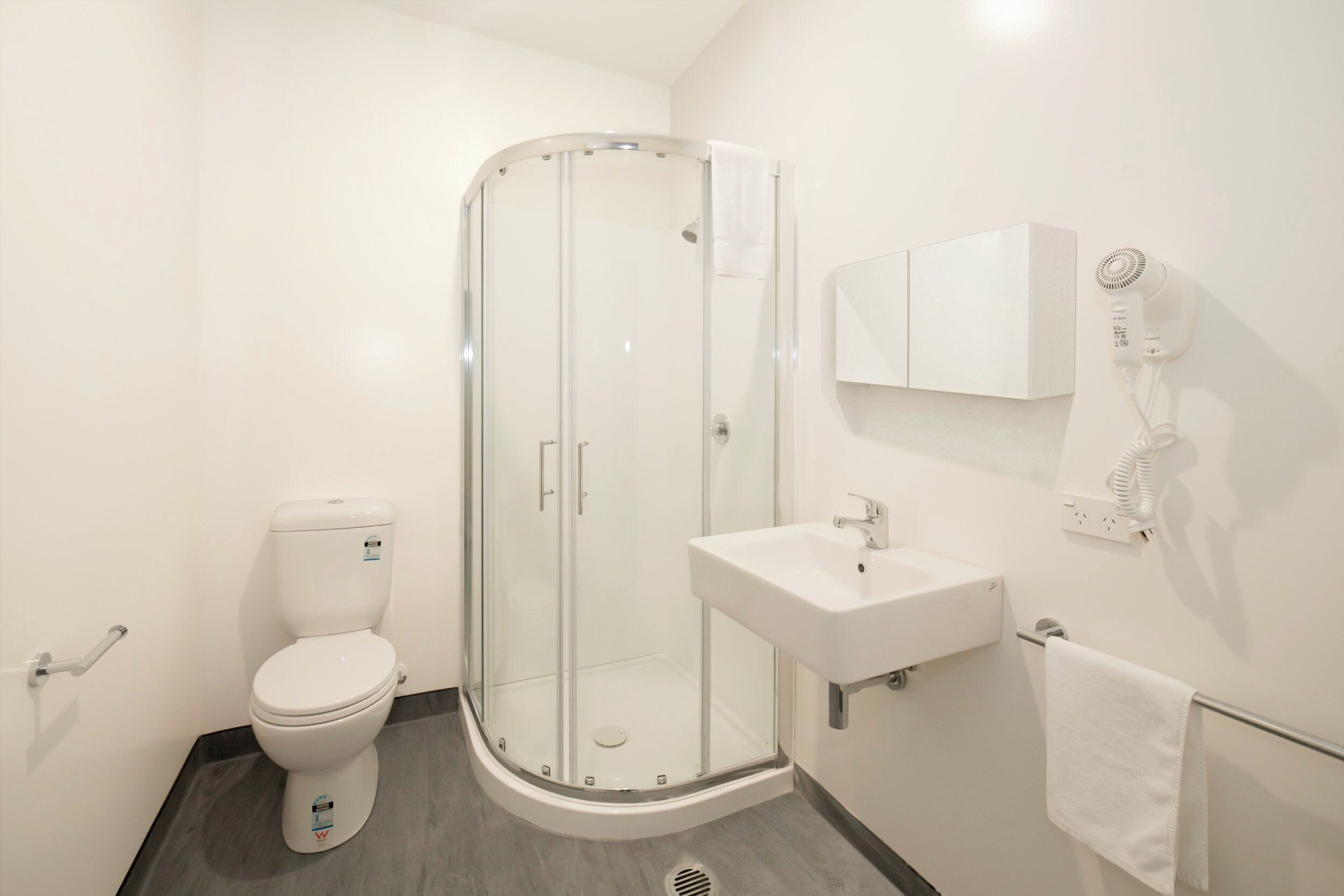Un baño moderno con ducha de vidrio, inodoro blanco y lavamanos con espejo.