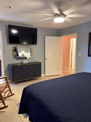 A bedroom with a bed, dresser, TV, and a ceiling fan.