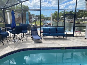 A poolside area with lounge chairs and a table, overlooking a body of water with boats.