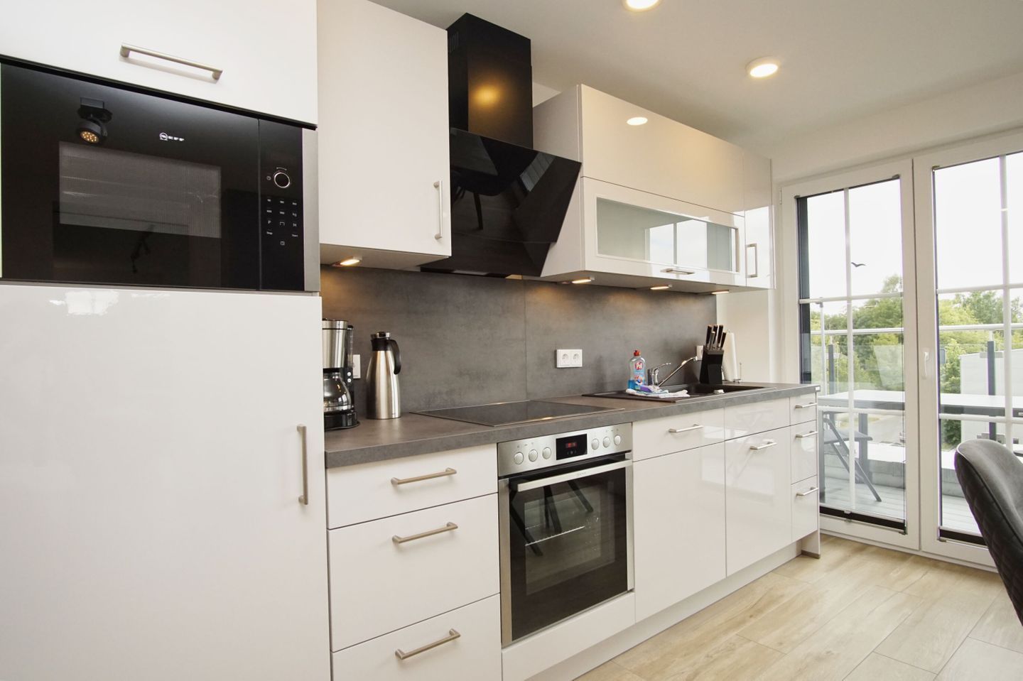 A modern kitchen with white cabinetry, stainless steel appliances, a built-in oven, and a large window offering a view of the outdoors.