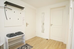 A room with a white door, a coat rack, a shelf with two gray cushions, and a welcome mat. - Alte Fischfabrik Lauterbach Penthousewohnung Nr. 13 Glücksmomente - Alte Fischfabrik (Putbus)