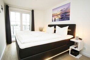Moderni makuuhuone, jossa on suuri sänky, yöpöytä ja taulu, jossa on kuvattuna auringonlasku.