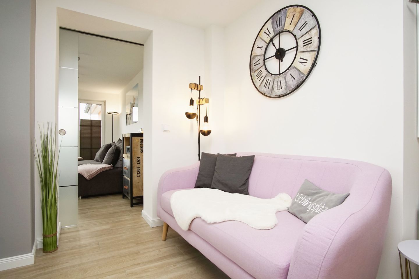 A modern living room with a pink sofa, a large wall clock, and a decorative light fixture.
