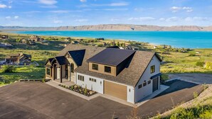 A modern two-story house with a garage, a driveway, and a view of a lake and mountains.