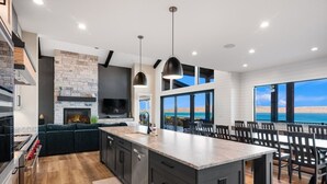 A modern kitchen with a stone fireplace, a large island, and a dining area with a view of the ocean.