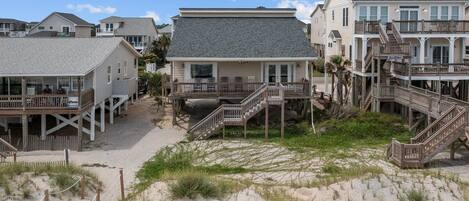 A beachfront property with multiple houses connected by walkways, featuring sandy grounds and grassy areas.
