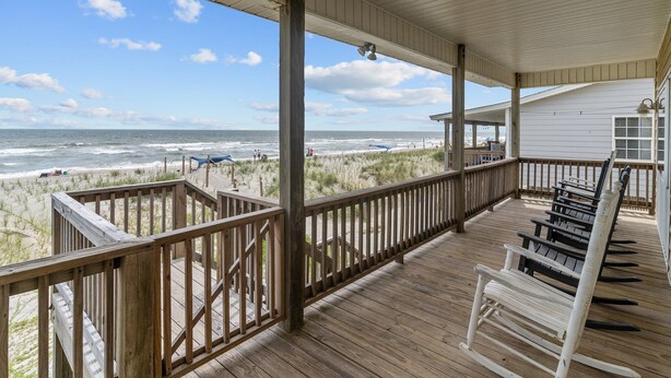 Een houten terras met een balustrade met uitzicht op een strand, met zicht op de oceaan en strandparasols.