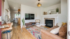 A living room with a fireplace, a TV, and a dining area in the background. - #HabitueHomes  - The Touchdown - Near BSU! (Boise)
