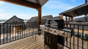 Een overdekt terras buiten met een grill en oven, met uitzicht op een woonwijk met huizen en een waterpartij.