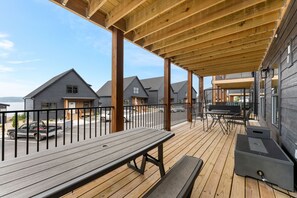 A wooden deck with a grill and seating area, overlooking a street with cars and houses. - Cedar Shores 7 Bedroom Home by RedAwning (Hollister)