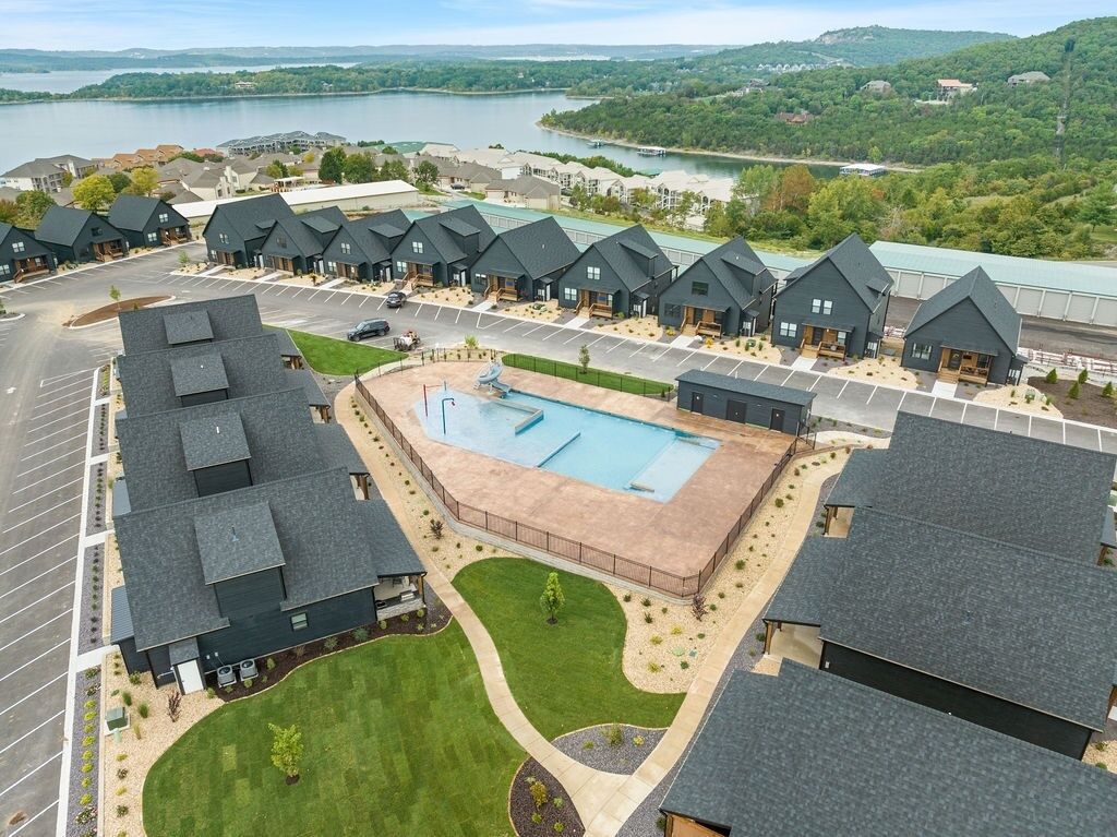 A residential area with multiple houses, a central swimming pool, and a view of a lake.