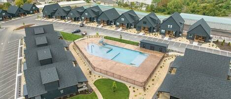 A residential area with multiple houses, a central swimming pool, and a view of a lake.