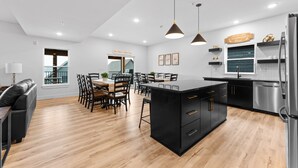 Een moderne keuken met een centraal eiland, zwarte kastjes, roestvrijstalen apparatuur en een eetgedeelte met houten stoelen en een tafel.