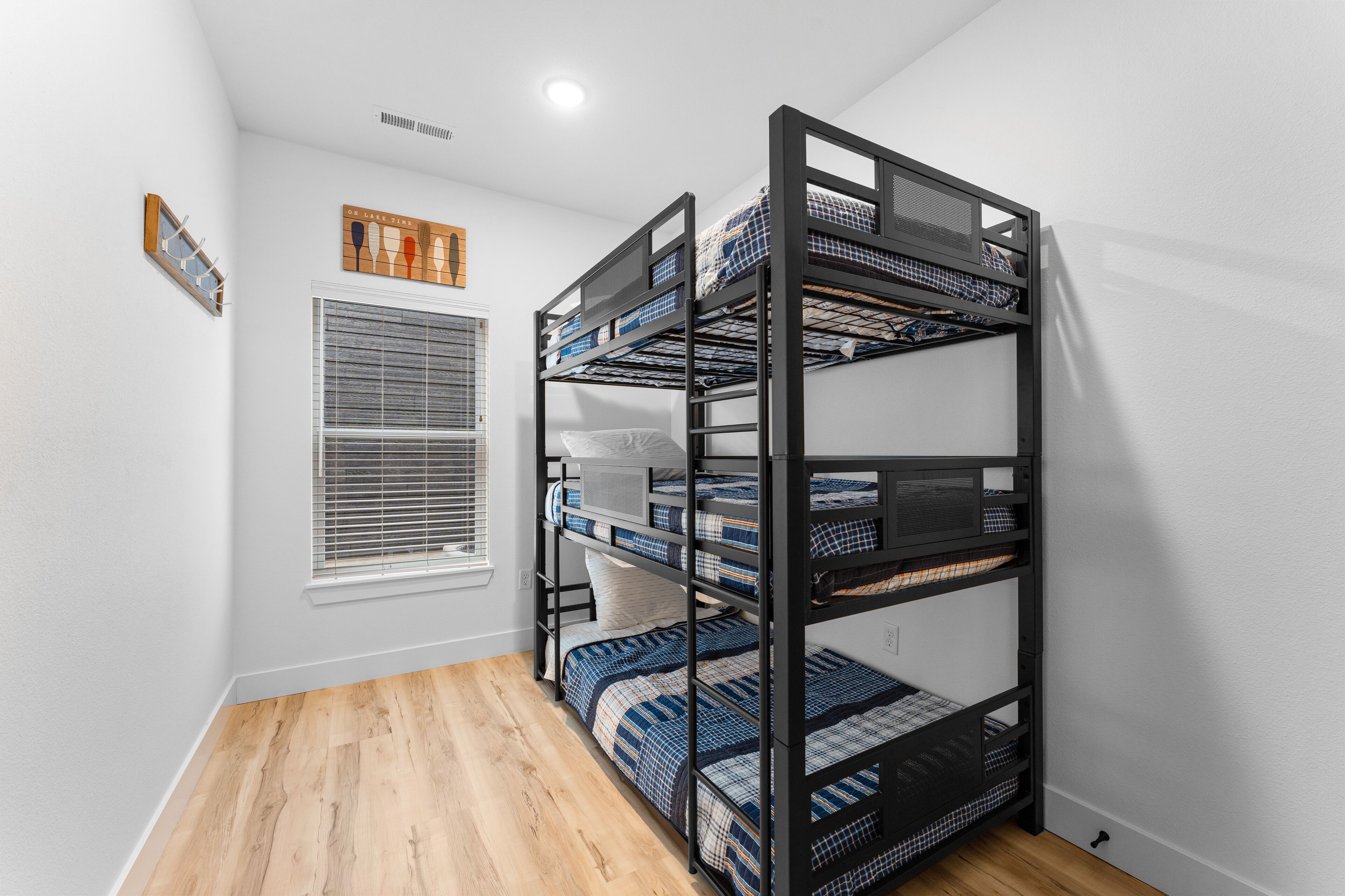 A bunk bed with multiple levels, a window with blinds, and a wooden floor.