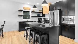 Een moderne keuken met zwarte kastjes, roestvrijstalen apparatuur en een centraal eiland met barkrukken.