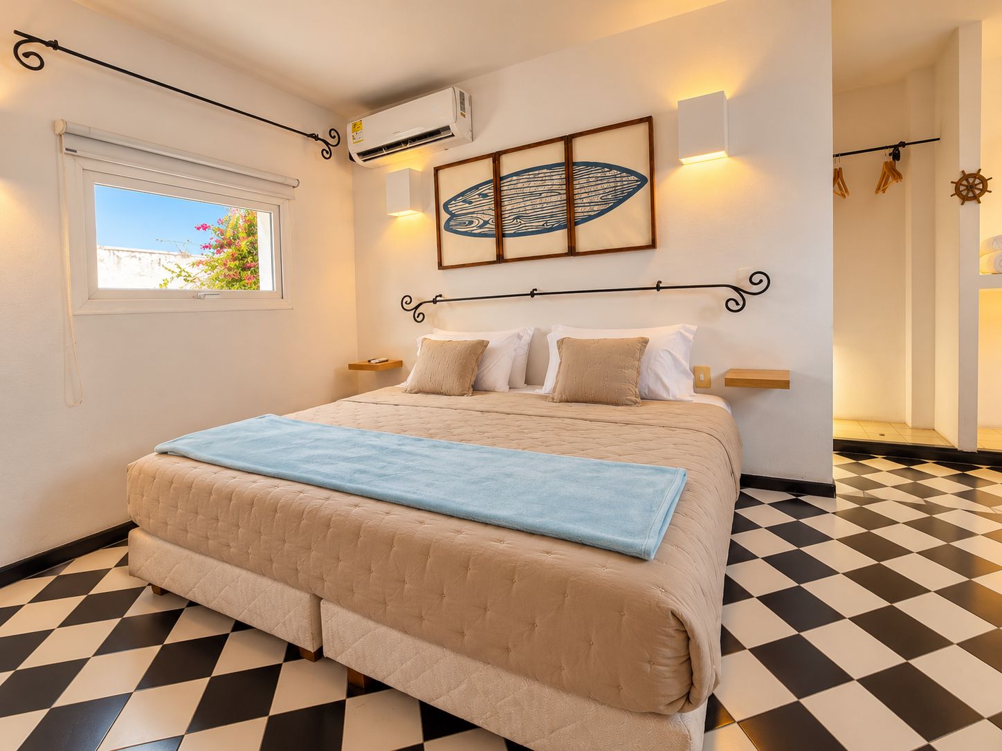 Une chambre d’hôtel avec un lit, une fenêtre, un appareil de climatisation, une œuvre d’art accrochée au mur et un sol à carreaux.