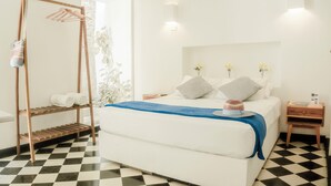 A bedroom with a bed, a wooden shelf with towels, a nightstand, and a window with a view of greenery. - 6 Bedroom Charming Colonial House With Pool (Santa Marta)