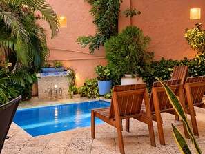 Zona de piscina amb una piscina blava, cadires de fusta i diferents plantes en testos.