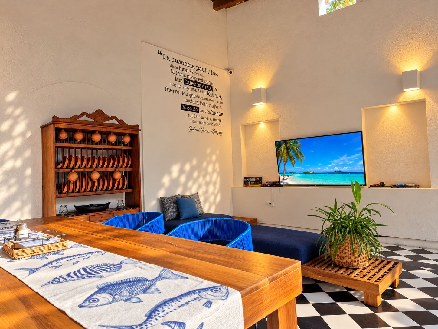 A room with a wooden dining table, blue chairs, a wall-mounted TV, and a decorative wall with text.
