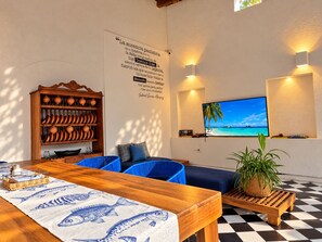A room with a wooden dining table, blue chairs, a wall-mounted TV, and a decorative wall with text. - 6 Bedroom Charming Colonial House With Pool (Santa Marta)