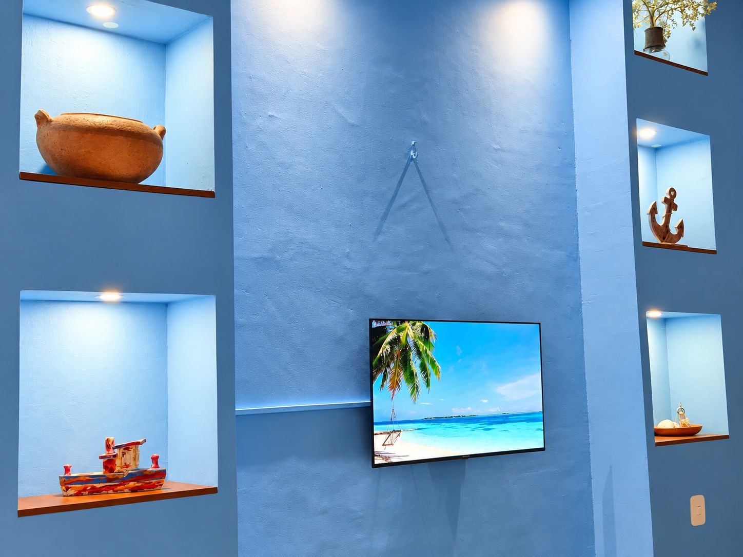 A room with a large flat-screen TV mounted on a blue wall, surrounded by shelves with various decorative items.