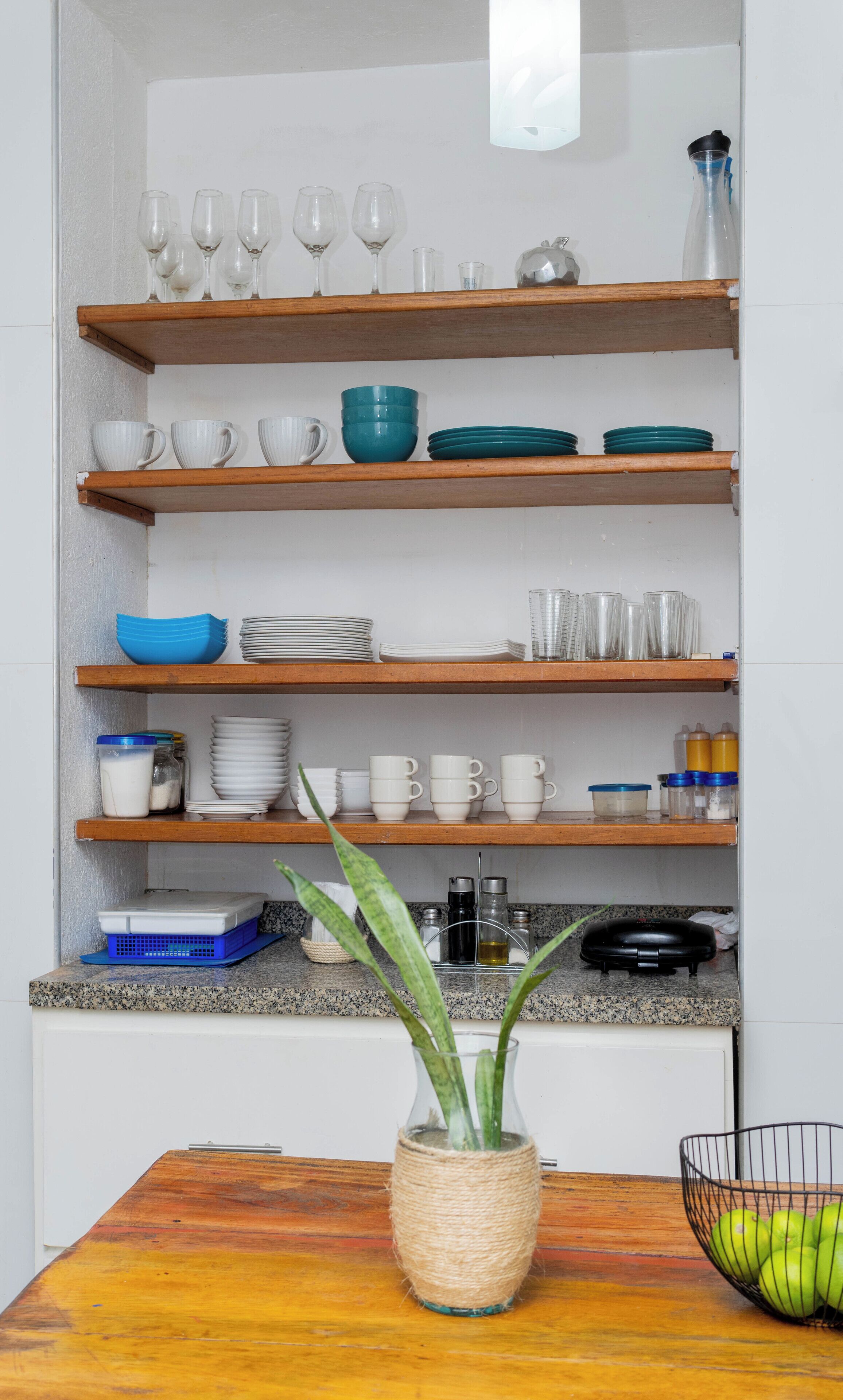 A kitchen with wooden shelves holding various dishes, cups, and a plant on the countertop.