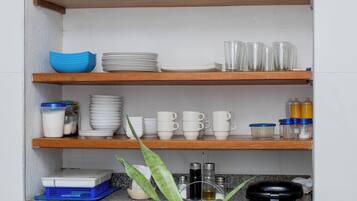 A kitchen with wooden shelves holding various dishes, cups, and a plant on the countertop.