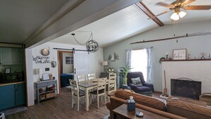 A spacious living room with a wooden floor, a dining area with a table and chairs, a fireplace, and a ceiling fan.
