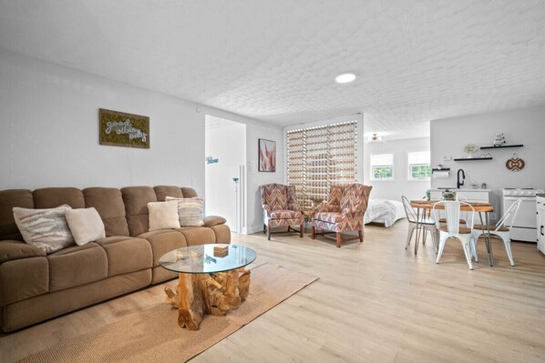 A modern living room with a brown sofa, a glass coffee table, and patterned armchairs.