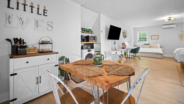 A modern, well-lit room with a wooden dining table, white cabinetry, and a kitchen area with appliances. - Luxury pet-friendly remodeled cottage (Sparta)