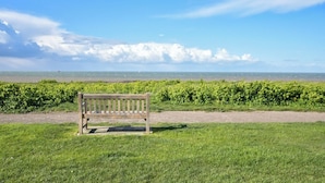A bench in a grassy area with a view of the sea and clouds in the sky.
