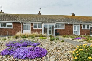 A two-story brick house with a tiled roof, a front door, and a small garden with purple and yellow flowers. - Amazing Beachside 2BD Family Home with Garden (Cliftonville)