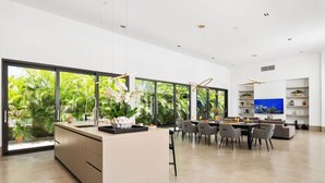 Een moderne keuken met een groot schiereiland, een eethoek met stoelen, en een televisie aan de muur.