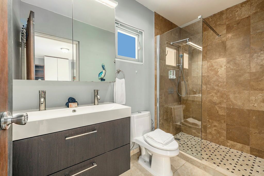 Un bagno moderno con uno specchio grande, un lavandino bianco, mobili scuri, un water e un box doccia in vetro.
