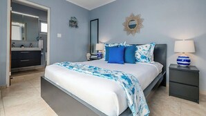 Una camera da letto con un letto, comodini, uno specchio e un bagno con lavandino e porta asciugamani.