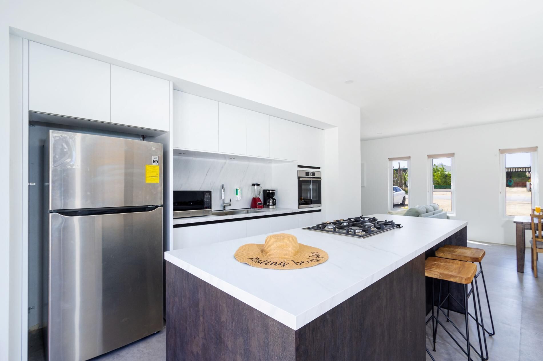 A modern kitchen with a stainless steel refrigerator, a microwave, an oven, and a gas stove. There is a large island with a hat and stools.