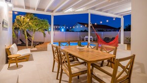 An outdoor patio with a wooden table and chairs, a pool, and a hammock. - Beautiful 3BR2BA, Amazing Location w/ Private Pool (Noord)