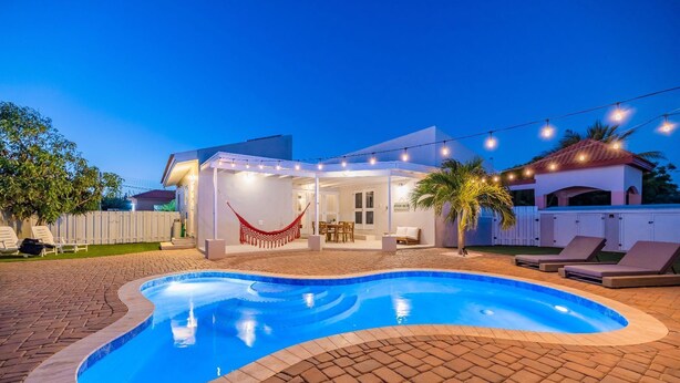 A swimming pool with a covered patio area, lounge chairs, and string lights. - Beautiful 3BR2BA, Amazing Location w/ Private Pool (Noord)