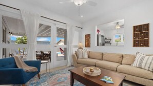 A living room with a blue armchair, beige sofa, and a wooden coffee table. There is a patterned rug on the floor, and a ceiling fan is visible. - Beautiful 3BR2BA, Amazing Location w/ Private Pool (Noord)
