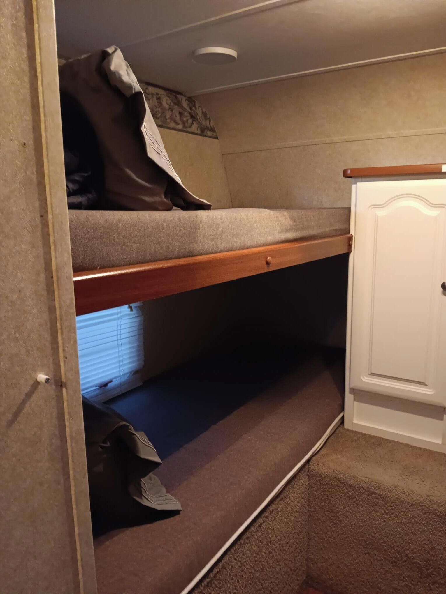 Un lit superposé avec une tête de lit en bois, une armoire blanche et un sol recouvert de moquette.