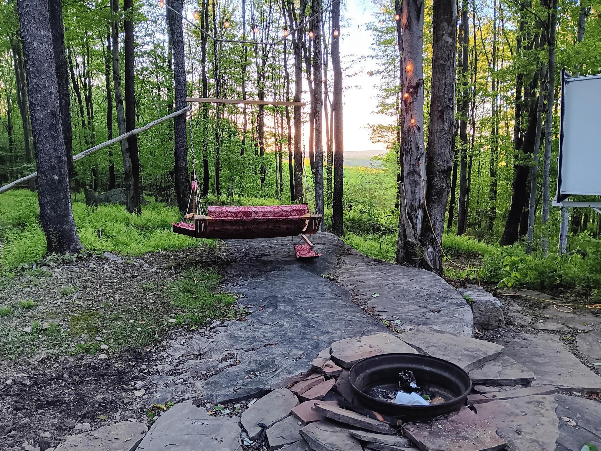 A rustic outdoor setting with a swing, a fire pit, and a stone pathway.